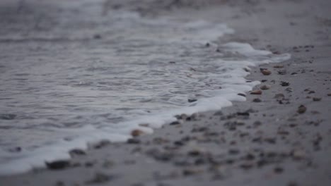 Slow-motion,-ocean-tide-washing-ashore-over-beach-full-of-seashells-and-small-rock