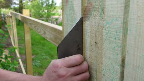 Person-measuring-fence-plank-and-using-pneumatic-nail-gun-to-build,-close-up