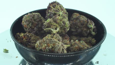 Close-up-shot-of-a-Marijuana-sativa-Sour-Diesel-flowers-with-trichomes,-green-and-purple-Kush-on-a-rotating-stand,-in-a-black-shiny-bowl,-Slow-motion-4K-video