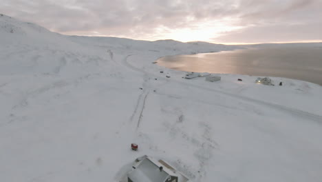Dolly-forward-towards-farm-covered-in-snow-on-ocean-shore,-Iceland