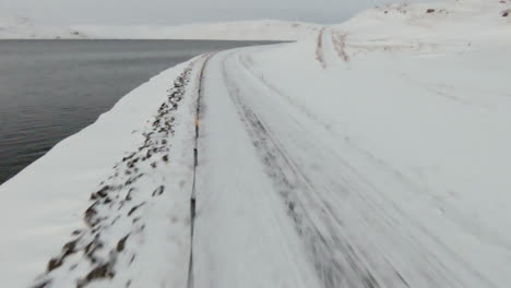 Snowy-country-road-along-ocean-shore,-dolly-forward