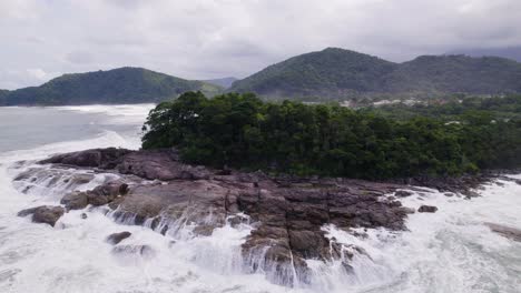 Drone-go-up-showing-a-rock-where-waves-break-and-the-atlantic-rainforest-in-the-background