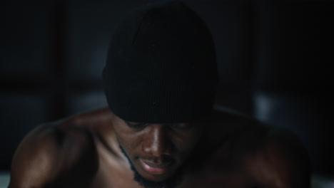 Young-black-male-wearing-beanie-cap-sitting-up-on-bed-giving-a-moody-look,closeup-shot