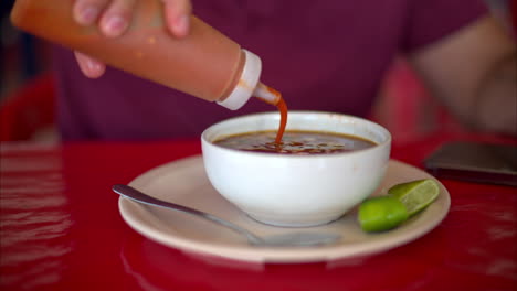 Slow-motion-close-up-of-a-latin-man-adding-red-hot-chilli-sauce-to-his-barbacoa-broth-in-a-restaurant-in-Mexico