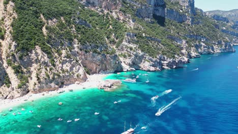 Boat-Tour-Excursions-and-Tourists-at-Cala-Mariolu-Beach,-Baunei-Coast,-Sardinia,-Italy---Aerial-4k