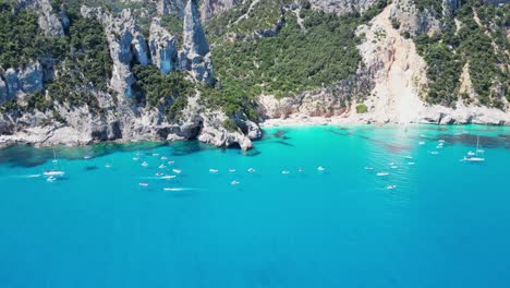 Touristenboote-Genießen-Sommerferien-An-Den-Felsformationen-Des-Strandes-Von-Cala-Goloritze-In-Sardinien,-Italien---4k-neigungsenthüllung-Aus-Der-Luft