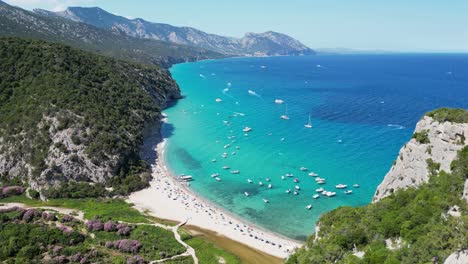 Boats-and-Tourists-at-Cala-Luna-Beach,-Baunei-Coast,-Sardinia,-Italy---Aerial-4k-Dolly