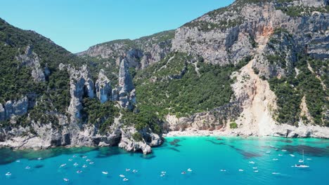 Tourist-Boats-Enjoy-Summer-Vacation-at-Cala-Goloritze-Beach-Rock-Formations-in-Sardinia,-Italy---Aerial-4k