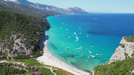 Boats-and-Tourist-People-at-Cala-Luna-Beach,-Baunei-Coast,-Sardinia,-Italy---Aerial-4k