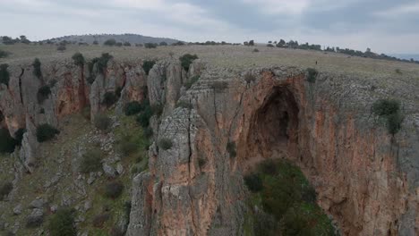 Imágenes-De-Drones-De-Un-Hombre-En-La-Distancia-Caminando-Sobre-Un-Acantilado-Rocoso-Y-Una-Cueva,-Israel