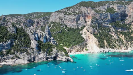 Touristenboote-Genießen-Sommerferien-Am-Strand-Von-Cala-Goloritze-Und-Felsformation-In-Sardinien,-Italien---4k-Luftkreisen