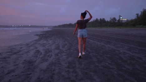 Landschaftsansicht-Einer-Jungen-Frau,-Die-Während-Eines-Violetten-Sonnenuntergangs-An-Einem-Sandstrand-Am-Meer-Spazieren-Geht,-Während-Sie-Ihre-Haare-Vereint