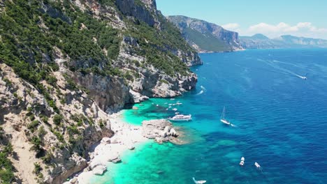Boat-Tour,-Tourist-People-and-Sandy-Beach-at-Baunei-Coast,-Sardinia,-Italy---Aerial-4k-Tilting-Down