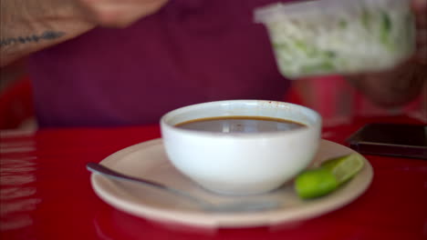 Slow-motion-close-up-of-a-latin-man-adding-chopped-onion-and-cilantro-to-his-barbacoa-broth-in-a-restaurant-in-Mexico