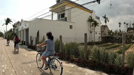 Frauen,-Die-In-Einer-Kleinen-Vietnamesischen-Stadt-Zwischen-Reispasteten-Fahrrad-Fahren