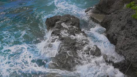During-the-day,-the-deep-blue-water-is-visible-as-it-crashes-against-the-rocky-shore,-the-whitecaps-and-spray-created-by-the-impact-in-slow-motion-give-a-stunning-visual-of-the-ocean's-strength