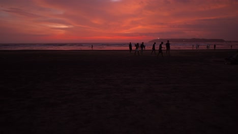 -Group-of-young-people-walking-on-sand-and-leaving-the-beach-at-dusk-with-red-sky