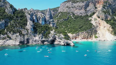 Tourist-Boats-Relax-at-Summer-Vacation-in-Cala-Goloritze-Beach,-Sardinia,-Italy---Aerial-4k-Circling