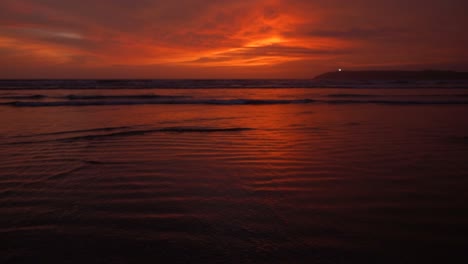 Calm-tidal-waves-coming-in-and-receding-at-the-shore-of-a-beach-at-sunset-with-red-sky