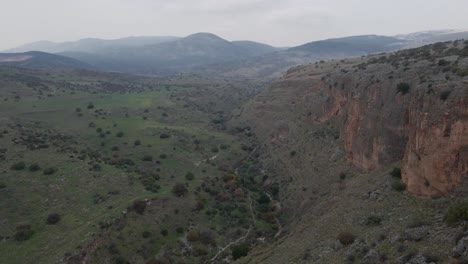 Vista-Aérea-De-Un-Excursionista-Masculino-Escalando-La-Ladera-De-Una-Montaña-Rocosa-Sobre-El-Valle,-Israel