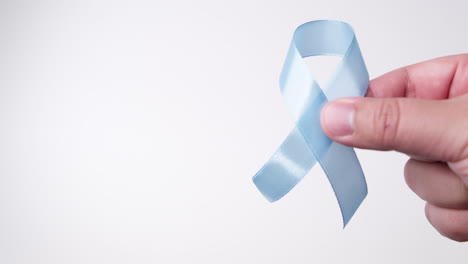 Detail-of-male-hand-placing-ribbon-in-light-blue-color-on-white-background