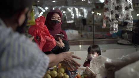 A-housewife-with-a-mask-while-shopping-for-various-vegetables-at-the-central-market-shows-late-payment-with-online-transactions,-and-the-seller-gives-the-vegetables-she-bought,-covid-19-situation