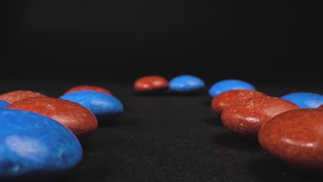 Macro-push-in-shot-of-button-shaped-red-and-blue-candy-with-a-black-background