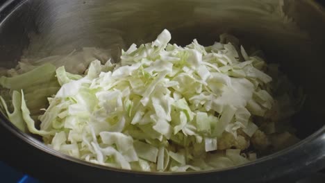 Chopped-Carrots-Being-Dropped-Over-Chopped-Cabbage,-Followed-By-Dry-Rice-And-Salt-Into-Metal-Bowl-In-Preparation-For-Vegetable-Stew