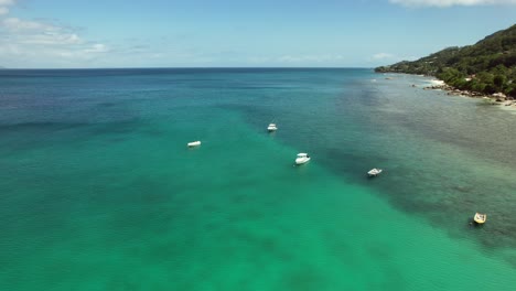 Drone-shot-of-boats-docking-near-beau-vallon-beach,-calm-sea-and-sunny-day,-clear-water