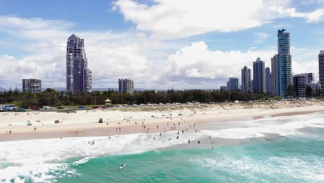Surfers-Paradise,-New-South-Wales,-Australia---February-28,-2021:-Aerial-over-swimmers-to-the-shallows-with-Gold-Coast-high-rise-in-buildings-in-the-background