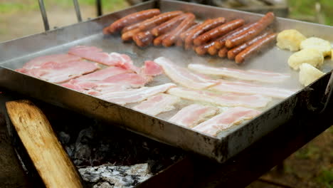 Bacon-and-sausages-being-fried-on-pan-on-open-fire---campsite-breakfast