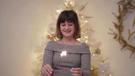 Ein-Mädchen-Beleuchtet-Weihnachtswunderkerzen-In-Zeitlupe-Mit-Baum-Im-Hintergrund