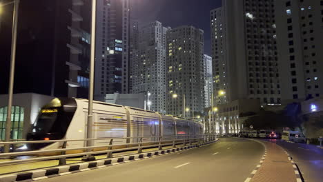 Moving-shot-of-a-street-in-Dubai-at-night-while-the-train-and-cars-are-passing-by