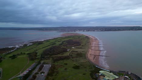 Early-morning-aerial-drone-flight-over-Dawlish-Warren-Spit-with-Exmouth,-Devon-in-the-distance-showing-narrow-entrance-to-the-River-Exe-and-the-Exe-Estuary-near-Exeter