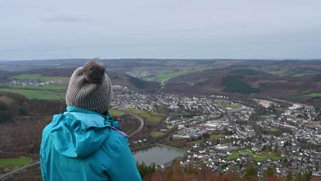 Earning-the-Sauerland-View:-A-Mid-aged-Woman-in-a-Blue-Jacket-and-Grey-Warm-Head-Enjoying-the-Olsberg-View-After-a-Long-Hike-on-a-Cloudy-Day