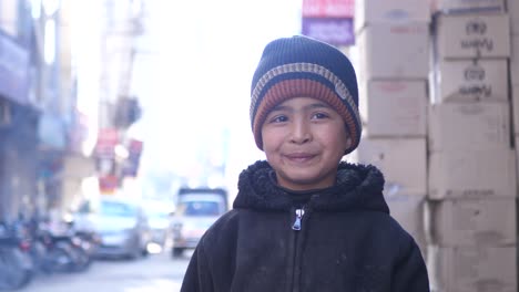 Niño-Varón-Joven-Con-Sombrero-Sonriendo-Mirando-Directamente-A-La-Cámara-En-La-Calle-En-Quetta,-Baluchistán