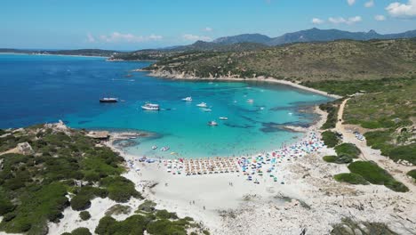 Punta-Molentis-Beach-in-Villasimius,-Sardinia---Tourist-People-and-Boats-Swim-and-Relax-in-Turquoise-Blue-Bay---Aerial-4k