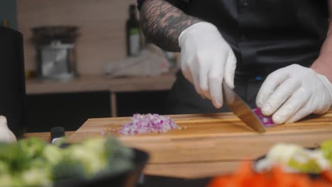 Fresh-red-onion-being-chopped-on-a-wooden-board-by-young-professional-male-chef-in-an-elegant-black-shirt-with-tattoos