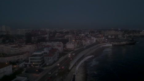 Aerial,-tracking,-drone-shot-panning-around-the-coast-of-Cascais-cityscape,-during-night-time,-in-Lisbon,-Portugal