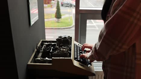 Portrait-Of-A-Person-Typing-On-Vintage-Manual-Typewriter-By-The-Window-With-Vehicles-Passing-By-Outside