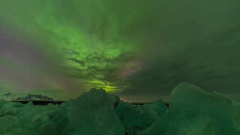 Aurora-bright-green-light-in-the-night-sky-over-the-ice-rock-block-in-the-north-sea-beach-in-Iceland-Norway-Nordic-country-cold-climate-in-winter-night-sky-photography-slow-motion-time-lapse-of-stars