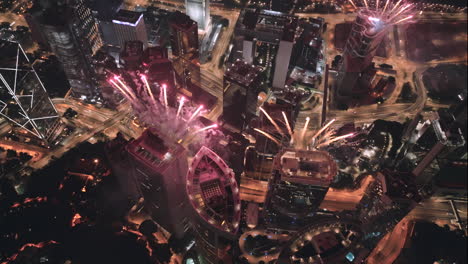 Circling-aerial-drone-shot-of-exploding-fireworks-on-top-of-high-rise-buildings-in-Hong-Kong-at-night