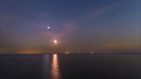 Moon-and-planet-is-setting-over-the-horizon-sky-line-and-the-sea-in-Persian-Arabian-Gulf-reflect-the-Moon-light-and-starry-night-sky-with-full-of-stars-Clouds-are-moving-oil-industry-light-time-lapse
