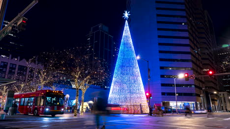 Time-lapse-of-the-Mile-High-Tree-lit-up-at-night-with-pedestrians-and-cars-quickly-passing-by-in-Denver,-Colorado