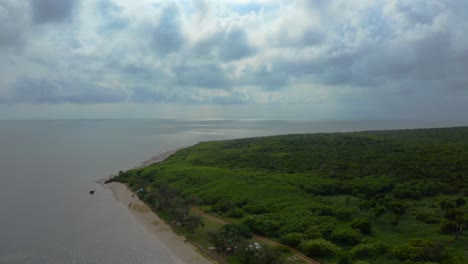 The-drone's-perspective-shifts-as-it-rises-above-the-tropical-beach,-providing-a-unique-and-captivating-look-at-the-surroundings-and-its-verdant-shore-on-a-cloudy-day