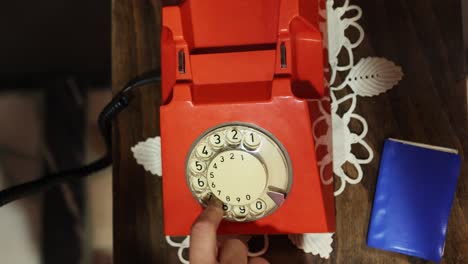 Teléfono-Rotatorio-Antiguo-Rojo-Sobre-La-Mesa-Con-Manos-Femeninas-Toma-El-Auricular-Y-Marca-Números