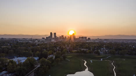 Aerial-timelapse-over-City-Park-in-Denver,-Colorado-with-the-sun-setting-behind-the-downtown-skyscrapers