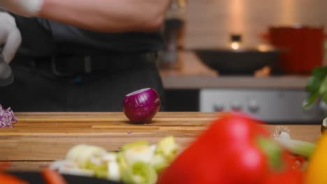 Fresh-red-onion-being-cut-on-a-wooden-board-by-young-professional-male-chef-in-an-elegant-black-shirt-with-tattoos