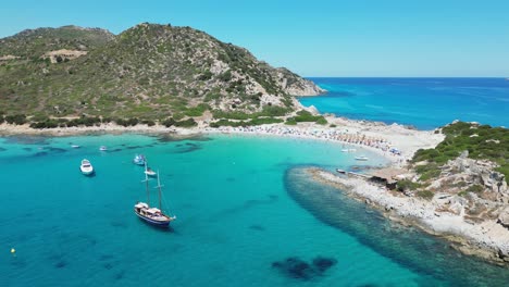Punta-Molentis-Beach-in-Villasimius,-Sardinia---Boats-and-Tourists-in-Turquoise-Blue-Sea-and-Small-White-Sandy-Beach---Aerial-4k-Circling