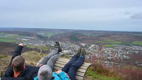 Golden-Years-in-the-Sauerland:-An-Elderly-Couple-Resting-on-a-Bench-and-Taking-in-the-Scenic-Town-View-of-Olsberg-on-a-Cloudy-Winter-Day